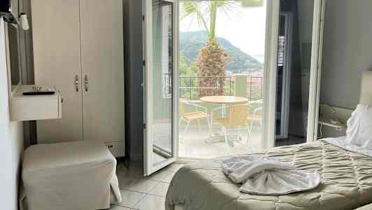 Hotellrom med utsikt mot en terrasse med bord, stoler og en palme. (AI-generert tekst)