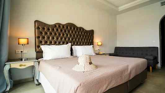 Et hotellrom med en dobbeltseng, en sofa og nattbord med lamper, samt en hatt plassert på sengen. (AI-generert tekst)