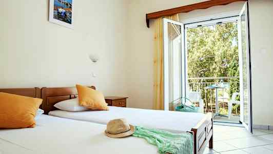 Et hotellrom med enkeltsenger, åpent vindu og utsikt mot balkong. (AI-generert tekst)