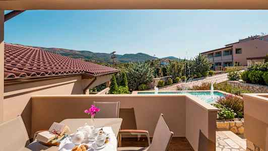 Utsikt fra en terrasse med bord og stoler, med en hage og fontene i bakgrunnen. (AI-generert tekst)