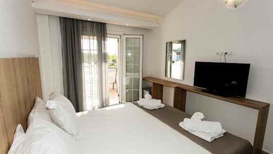 Et hotellrom med en dobbeltseng, en TV på en trebenk og en balkong med utsikt. (AI-generert tekst)