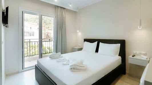 Et hotellrom med en dobbeltseng, hvitt sengetøy og et vindu som vender mot en balkong. (AI-generert tekst)