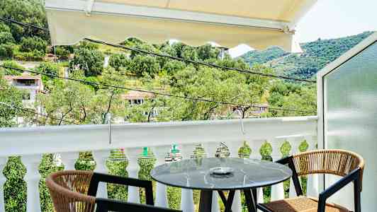 Utsikt fra en balkong med et lite rundt bord og to stoler, omgitt av grøntområder og et kupert landskap. (AI-generert tekst)