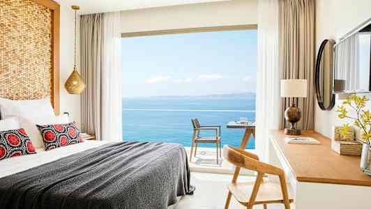 Et hotellrom med en oppredd seng, skrivebord og utsikt over havet gjennom vinduet. (AI-generert tekst)