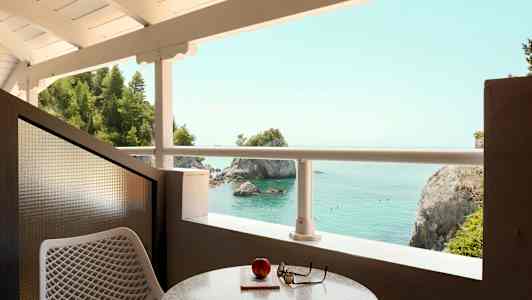 Utsikt fra en balkong mot havet med klipper og trær. (AI-generert tekst)