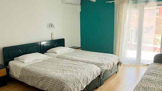 Et hotellrom med to enkeltsenger, en sofa og en balkongdør. (AI-generert tekst)