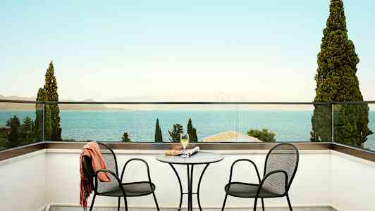 To stoler og et bord på en terrasse med utsikt mot havet. (AI-generert tekst)