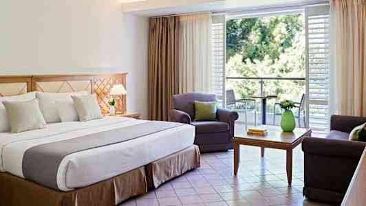 Interiør av hotellrom med dobbeltseng, sittegruppe og balkong. (AI-generert tekst)