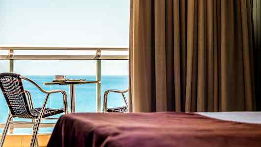 Rom med brun gardin, utsikt over havet og møblert balkong. (AI-generert tekst)