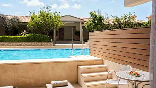 Utsikt fra en terrasse med solsenger og et bord med frukt, mot et basseng og hage. (AI-generert tekst)