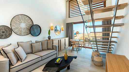 Et lyst og moderne rom med en sofa, trapper, veggdekorasjoner og utsikt mot en terrasse. (AI-generert tekst)
