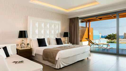 Et hotellrom med dobbeltseng, dagseng og utsikt mot en terrasse med basseng og hav. (AI-generert tekst)