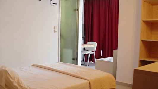 Et hotellrom med en seng, et bord og stoler, samt en hylle og røde gardiner. (AI-generert tekst)