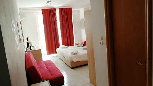 Et hotellrom med en oppredt seng, røde gardiner og en rød sofa. (AI-generert tekst)