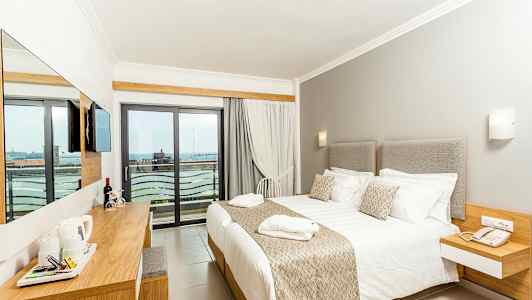 Et hotellrom med en stor seng, lyse møbler og en balkong med utsikt. (AI-generert tekst)