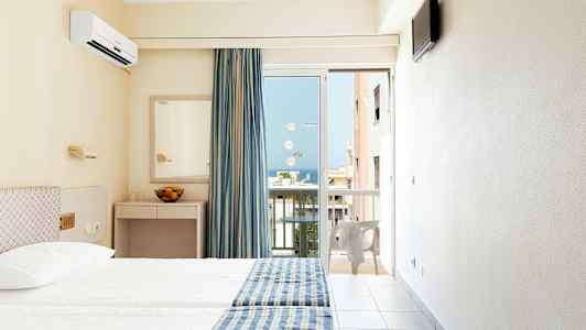 Hotellrom med to senger, blågule sengetepper, speil og en balkongdør med utsikt. (AI-generert tekst)