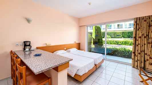 Et hotellrom med to senger, kjøkkenbar med sitteplasser og stor glassdør mot en hage. (AI-generert tekst)