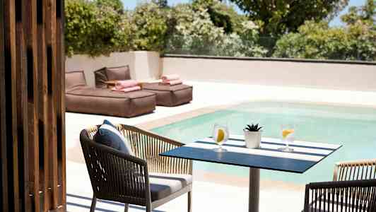 Et bord med to glass vann og en liten plante ved et basseng, med solsenger i bakgrunnen. (AI-generert tekst)