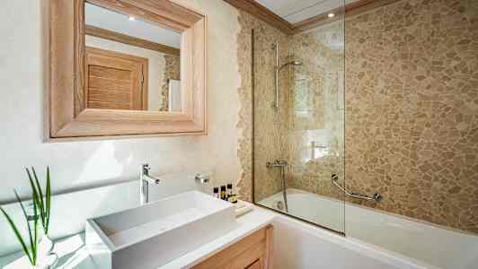 Et bad med en servant, et speil med treramme og et badekar med mosaikkvegg og dusj. (AI-generert tekst)