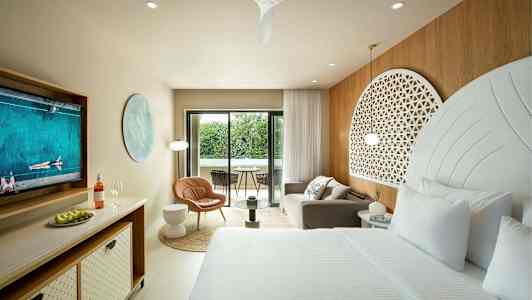 Et elegant hotellrom med en stor seng, sittegruppe og en balkong med utsikt over grøntområder. (AI-generert tekst)