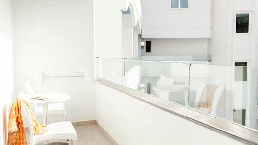 Hvit balkong med glassrekkverk, et bord og to stoler. (AI-generert tekst)