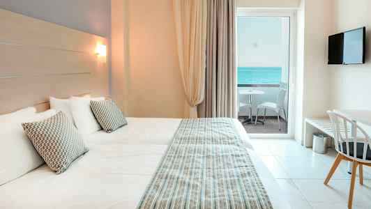 Hotellrom med to senger, utsikt over havet fra balkongen. (AI-generert tekst)