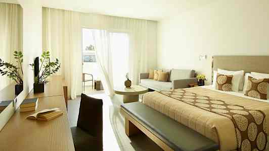 Moderne hotellrom med dobbeltseng, sofa og bord, samt balkong. (AI-generert tekst)