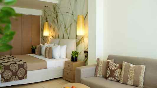 Et hotellrom med en seng, sofagruppe og bord dekorert med puter og frukt. (AI-generert tekst)