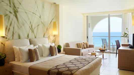 Hotellrom med havutsikt og moderne innredning inkludert seng, sofa og balkong. (AI-generert tekst)