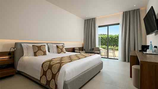 Et hotellrom med en stor oppredd seng, sittegruppe og glassdør til terrasse. (AI-generert tekst)