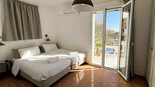 Hotellrom med to enkeltsenger, åpne vinduer med utsikt til en terrasse. (AI-generert tekst)