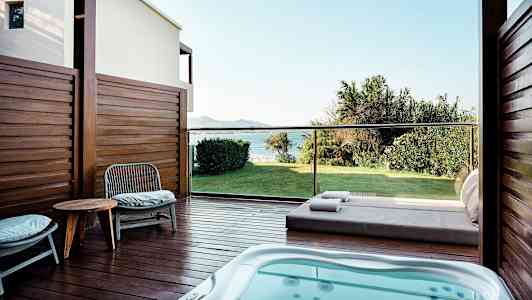 En terrasse med boblebad, stoler og et bord, utsikt over en grønn plen og havet. (AI-generert tekst)