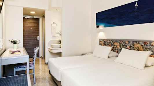 Et hotellrom med to hvite enkeltsenger, et skrivebord, en stol og en liten vask utenfor badet. (AI-generert tekst)