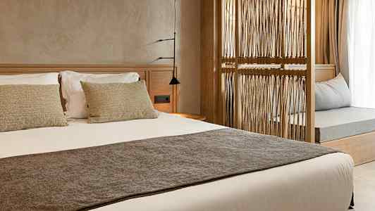 En hotellrominteriør med en oppredd seng og en dekorativ treramme som skiller rommet. (AI-generert tekst)