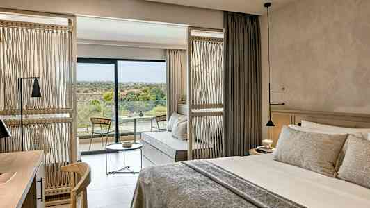 Hotellrom med en dobbeltseng, sittegruppe og en balkong med utsikt over natur. (AI-generert tekst)