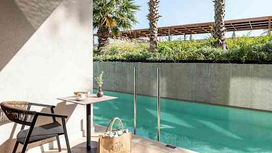 En sittegruppe med bord og stol ved et basseng med glassrekkverk. (AI-generert tekst)