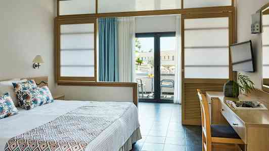 Hotellrom med en seng, skrivebord og balkong. (AI-generert tekst)