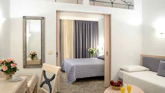 Hotellrom med to senger, et bord med to glass appelsinjuice, og et skrivebord med speil og blomster. (AI-generert tekst)