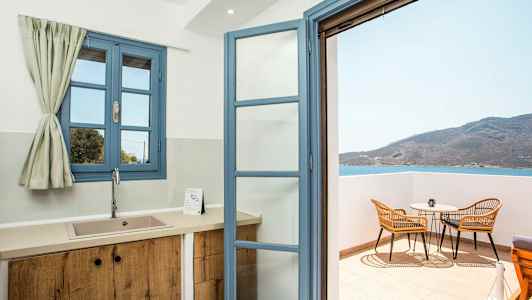 Et kjøkken med blå vinduer og en åpen dør til balkongen med utsikt over havet. (AI-generert tekst)