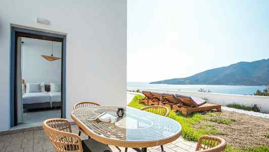 Utemøbler med bord og stoler foran en romåpning og solsenger i en hage med utsikt mot havet. (AI-generert tekst)