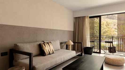 En stue med sofa, salongbord og store vinduer som vender mot en balkong. (AI-generert tekst)