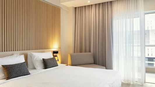 Soverom med en dobbeltseng, trepanel på veggen og store vinduer med lyse gardiner. (AI-generert tekst)