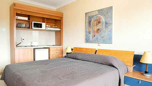 Et rom med en seng, et lite kjøkken og et veggmaleri. (AI-generert tekst)