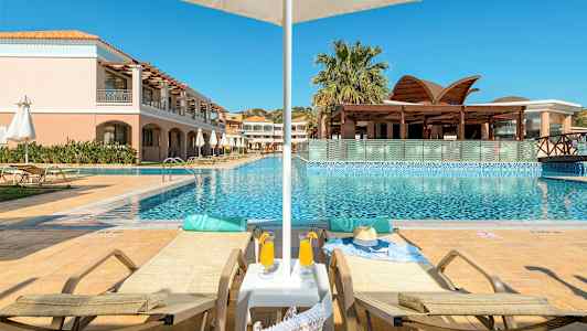 To solsenger ved et basseng med parasoll og en bygning i bakgrunnen. (AI-generert tekst)