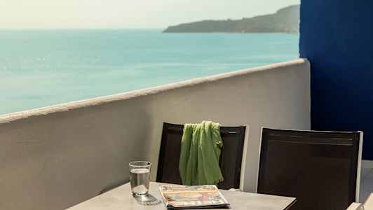 To stoler med et grønt teppe på den ene, stående ved et bord som har et vannglass og en avis, med havutsikt. (AI-generert tekst)