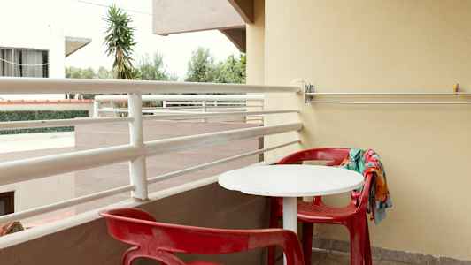 En balkong med røde stoler og et hvitt bord. (AI-generert tekst)