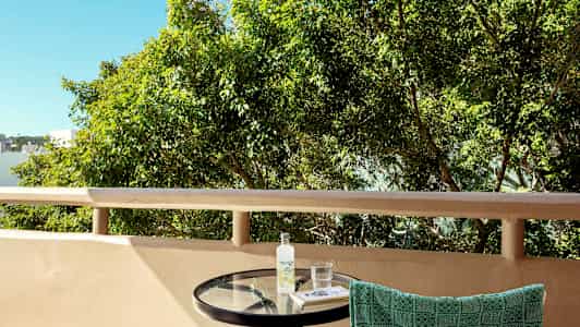 Bilde av en balkong med et rundt bord, et håndkle hengende på stolryggen, samt trær i bakgrunnen. (AI-generert tekst)