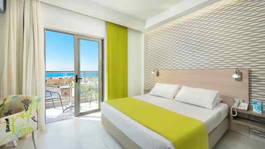 Et hotellrom med en seng, grønt sengeteppe, lyse møbler og en balkong med havutsikt. (AI-generert tekst)