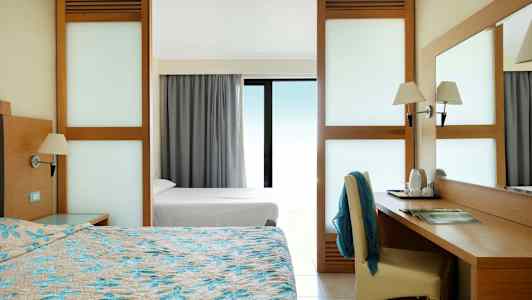 Hotellrom med dobbeltseng, skrivebord og utsikt gjennom et vindu med glass. (AI-generert tekst)