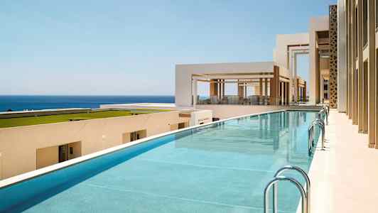 Bilde av et basseng ved et moderne, lyst byggkompleks med utsikt over havet. (AI-generert tekst)